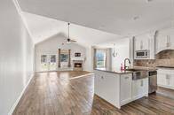 This is a spacious, open-concept living area with a modern kitchen featuring stainless steel appliances and granite countertops. It includes a cozy fireplace in the living room and has high vaulted ceilings with a ceiling fan. The space is well-lit with natural light from large windows and a glass door leading outside.