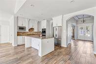 This is a modern kitchen featuring white cabinetry, granite countertops, stainless steel appliances, a tile backsplash, and wood flooring.