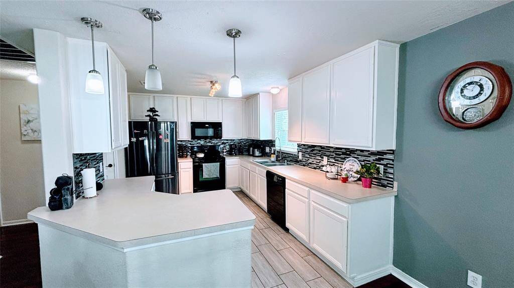 This kitchen features a white cabinetry, a sleek tile backsplash, and stainless steel appliances. It has ample counter space, pendant lighting, and a functional layout, perfect for cooking and entertaining.