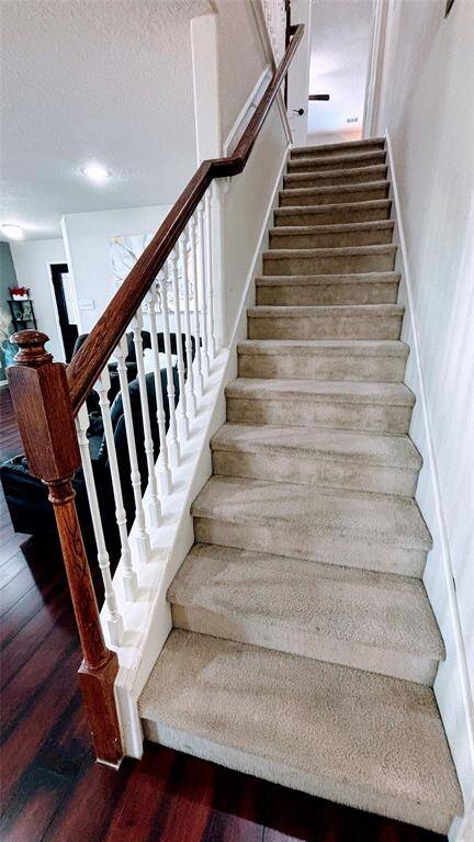 Carpeted staircase with white spindles and a dark wooden handrail, leading to an upper floor.