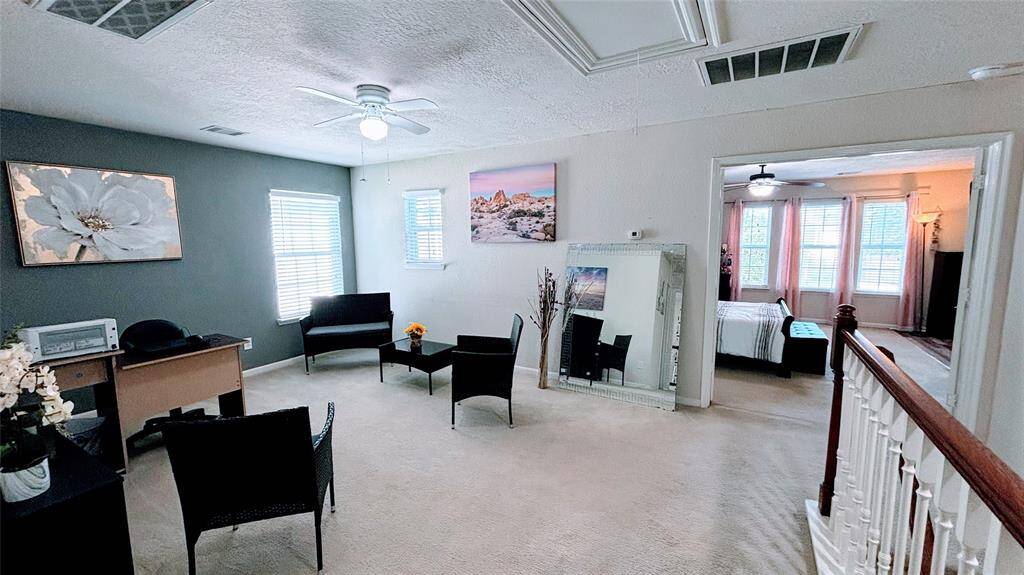Bright, carpeted upper landing area (Game room). It connects to the bedrooms with large windows. The space features neutral walls, a ceiling fan, offering a cozy and versatile living area.