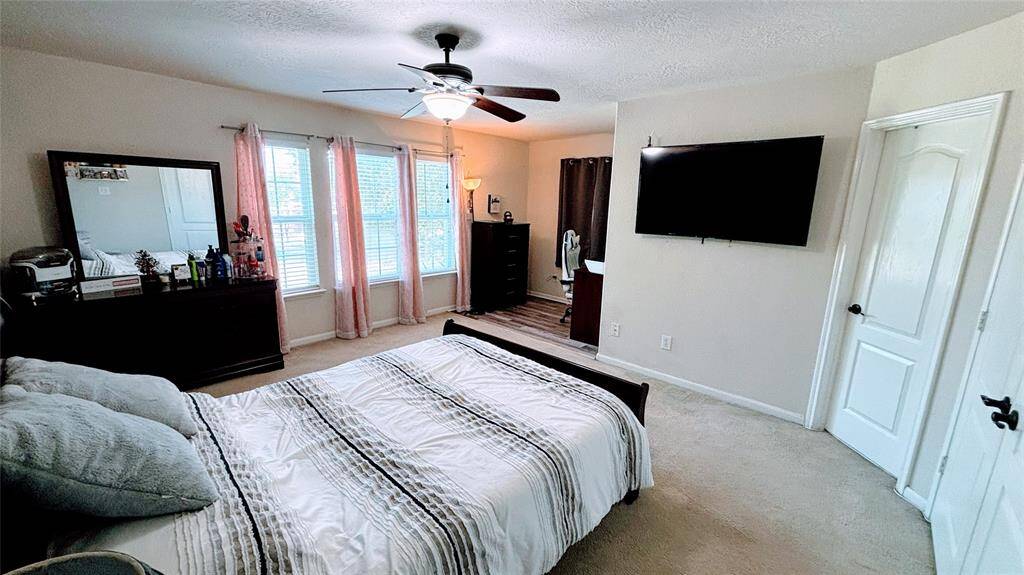 This is a bright Master bedroom featuring a large window with pink curtains, a ceiling fan, and carpeted floor with a double bed and ample storage.