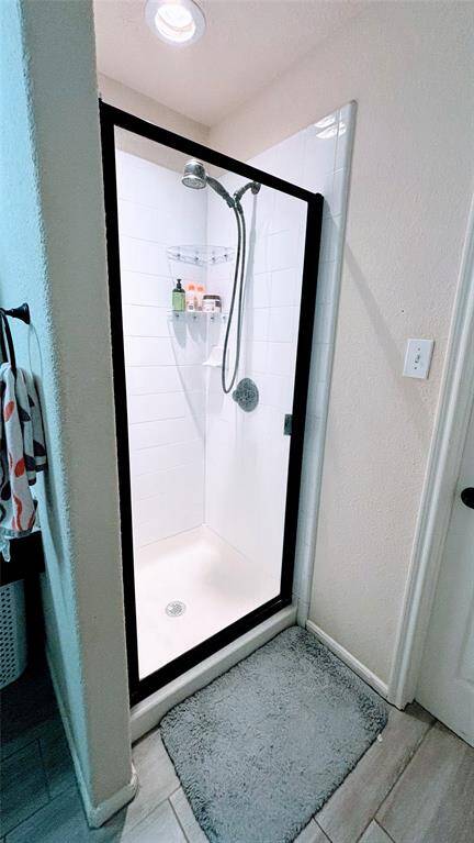 Modern shower with glass door and white tile, featuring a detachable showerhead. Includes built-in shelving for toiletries, and a cozy bath mat on tiled flooring.