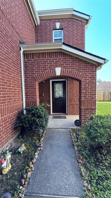 Welcoming brick exterior with a charming arched entryway. A well-maintained path leads to a stylish black front door, surrounded by manicured shrubs and a neat lawn.