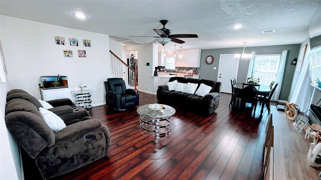 This spacious bright living area features rich hardwood floors and a ceiling fan. It seamlessly connects to a modern kitchen with a dining area, creating an inviting, open-concept space perfect for family gatherings.