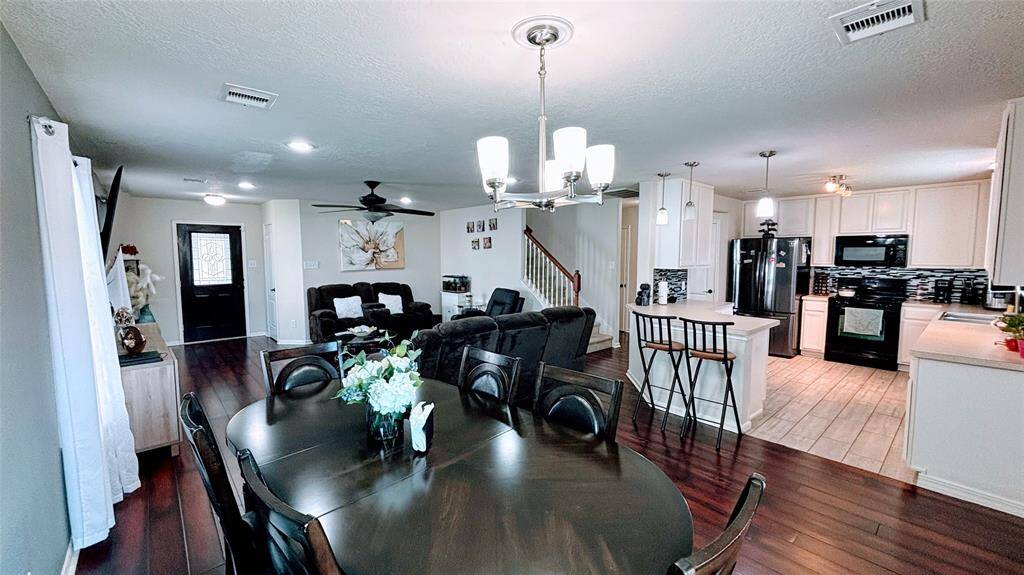 This open-concept living area features a modern kitchen with white cabinets and black appliances, a cozy living room with plush seating, and a dining area with a sleek table.