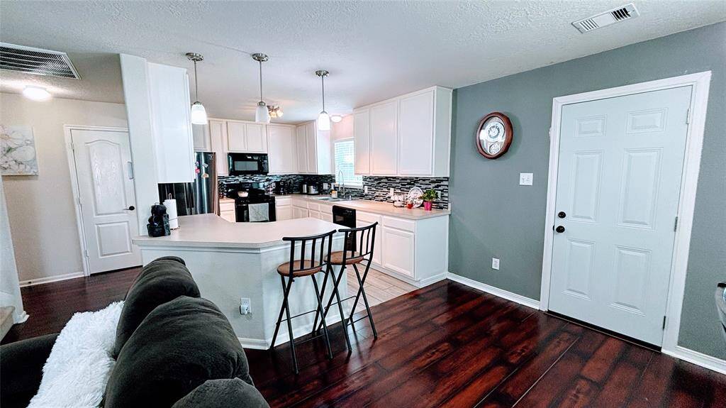 Modern kitchen with dark wood flooring and a cozy breakfast bar. The kitchen features white cabinetry, a stylish tile backsplash, and stainless steel appliances.