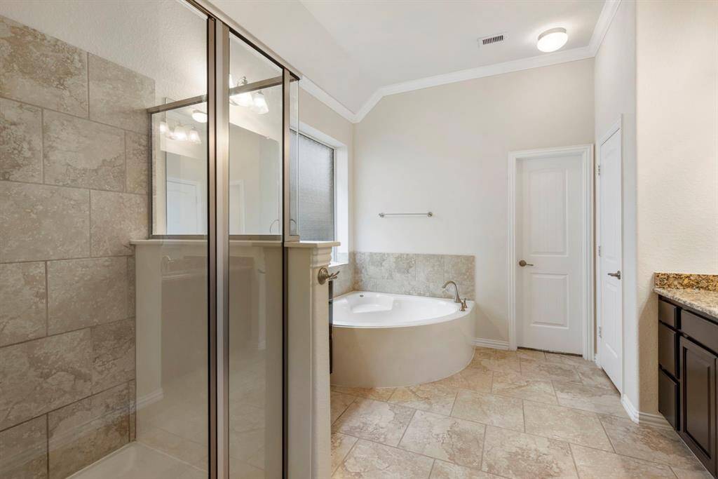 The corner jetted soaking tub and a large walk-in shower featuring a rain shower fixture, tile surround, and a seamless glass enclosure adds a modern touch.