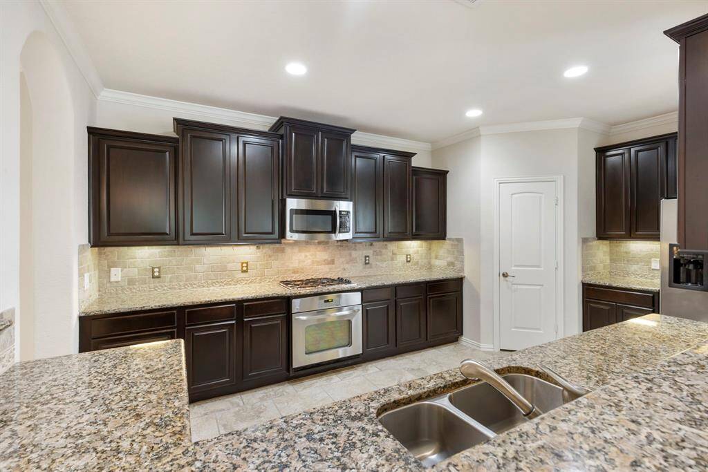 The impressive kitchen features rich, dark cabinetry that adds depth and warmth to the space. Expansive granite countertops provide ample workspace for meal prep and entertaining, beautifully complemented by a timeless stone backsplash.