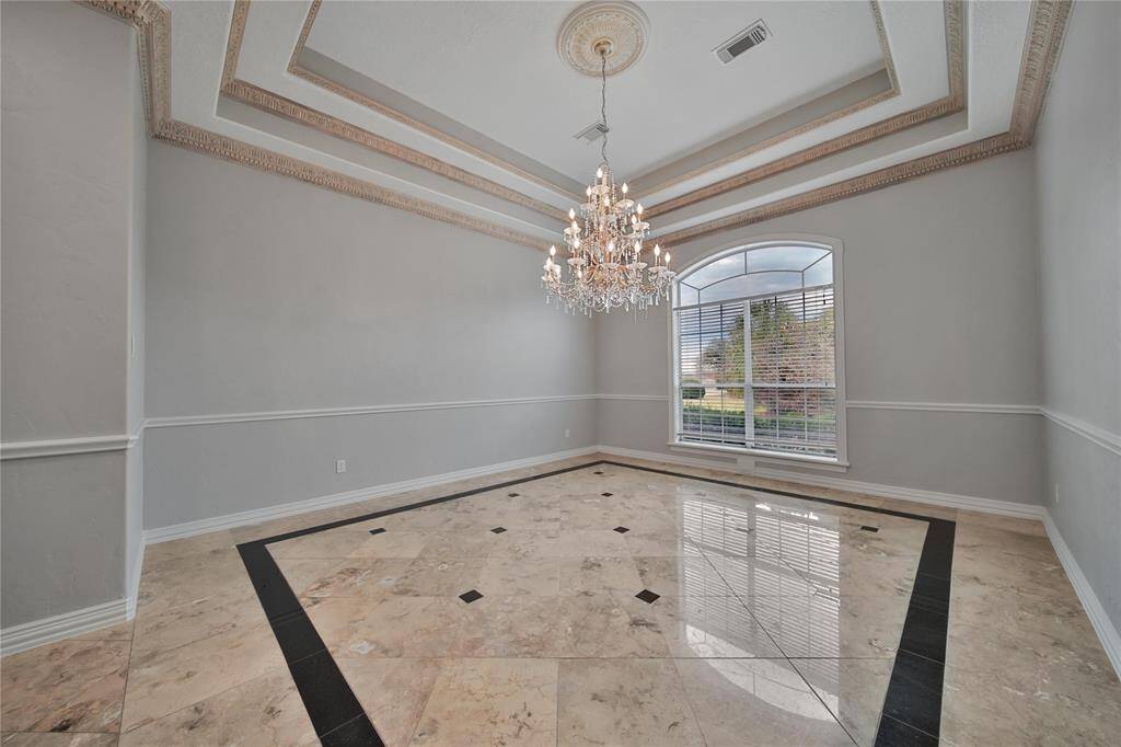 A formal dining room featuring tiered lighting, a stunning chandelier, and elegant marble floors.