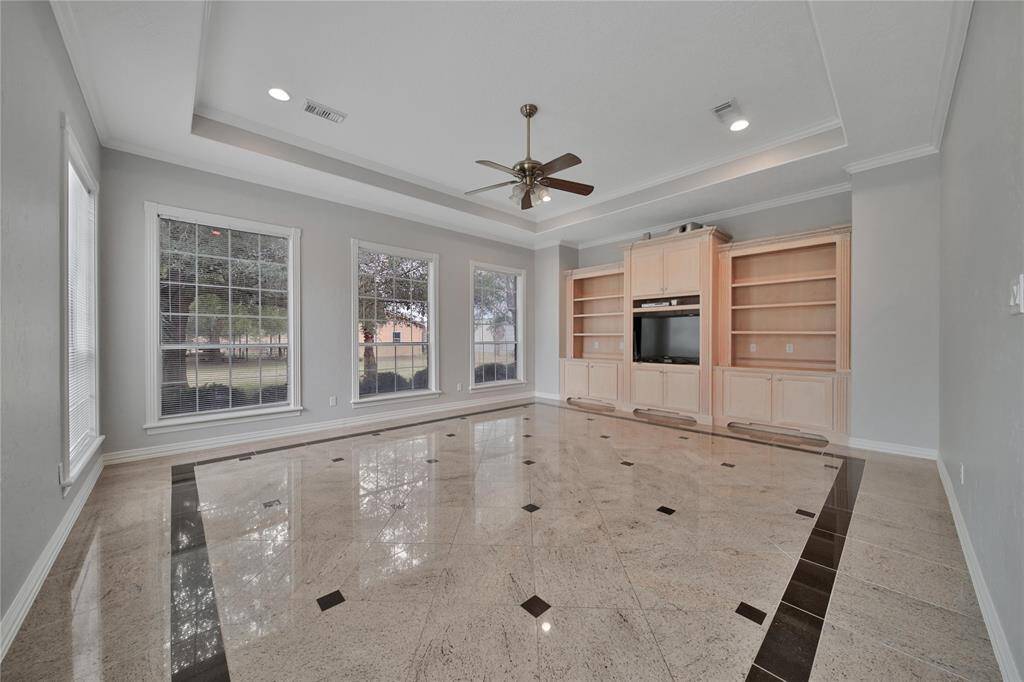 A spacious family room, complete with a built-in entertainment center and shelving, and featuring marble flooring.