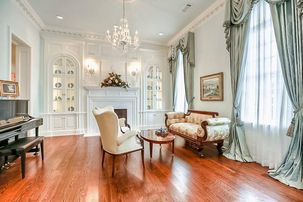 Formal living room straight out of the pages of a magazine. White River dentil trim, crown molding, paneled wall, and two paneled cased openings and a paneled arch for easy access from the foyer or main hallway. Shellback lighted cabinets and Schonbek crystal sconces. Wood burning fireplace with Sugar White Marble surround and custom mantle. Custom-made silk drapes inspired by Henrietta Spencer-Churchill "Georgian Style and Design".
