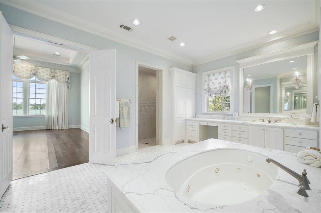 En suite Master bath has views of the lake from the window above the vanity and through the Owner's Retreat. Imagine soaking in the jacuzzi with these views! Calacatta Oro tub surround with multi-jet jacuzzi, Basketweave Marble floor continues the pattern into the large walk-in shower with duo seating areas. Built-in linen closet. Grohe thermostatic fixtures.
