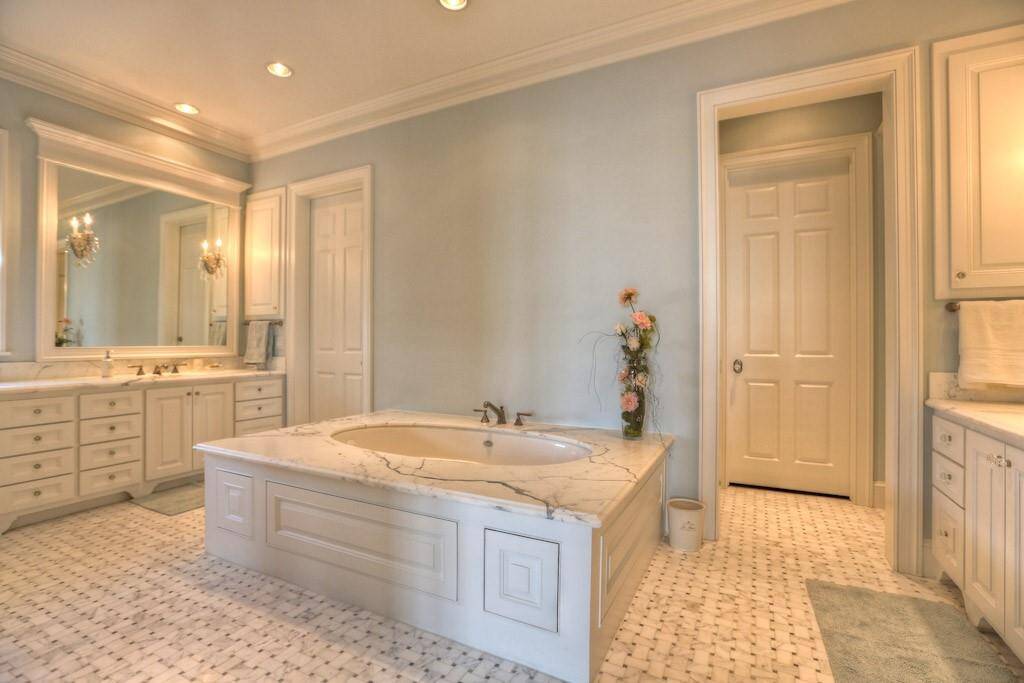 Separate "his" and "her" sinks. Left side sink has Calacatta Oro counter with built-in vanity. Built-in medicine cabinet, Schonbek crystal sconces integrated into the framed mirror with crown molding detail. Crystal knobs and hardware. Through the door is a massive walk-in closet with Carrara Marble packing island and dressing bench.