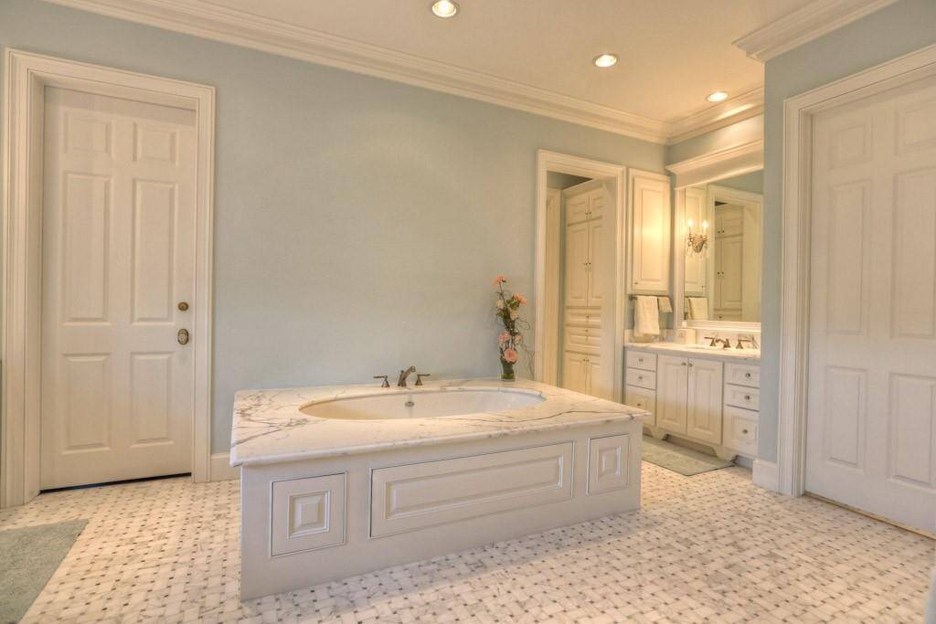 Right side sink has Calacatta Oro counter and built-in medicine cabinet. Schonbek crystal sconces integrated into framed mirror with crown molding detail. Crystal knobs and hardware. To the left of the sink is a small hallway that leads to a pair of floor-to-ceiling storage with separate hampers. Beyond is the second walk-in closet.