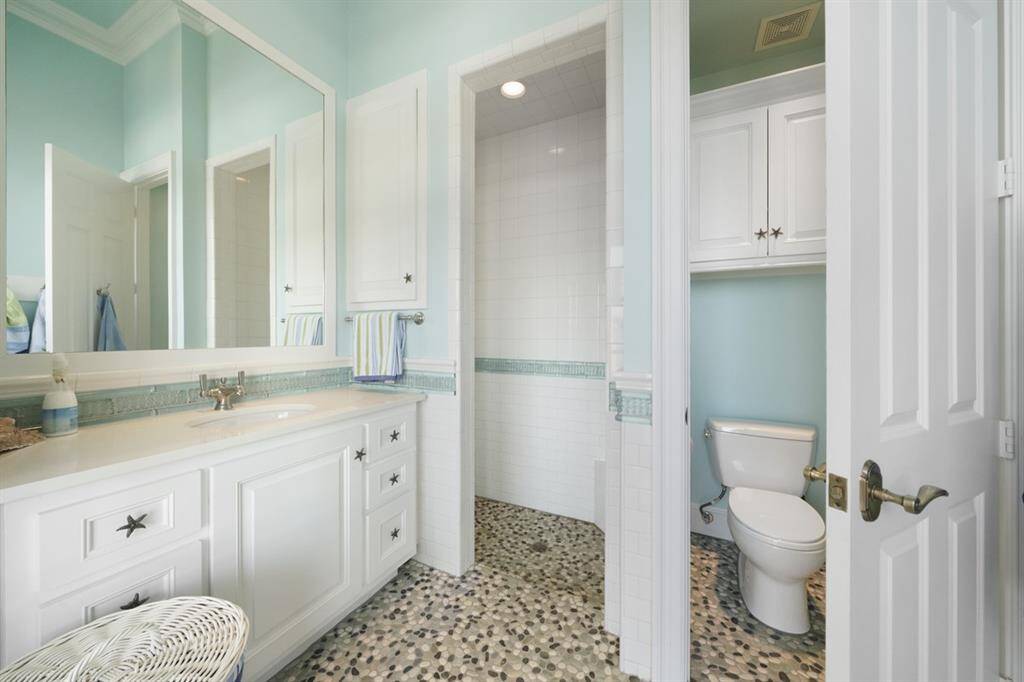 Pool bath inspired by the colors of a pristine ocean with aquatic detailing: starfish knobs, sea glass colored tile work, multiple hooks for towels and bathing suits, and pebble mosaic flooring. Subway tiled walk-in shower, built-in cubby, built-in medicine cabinet, and Kohler fixtures