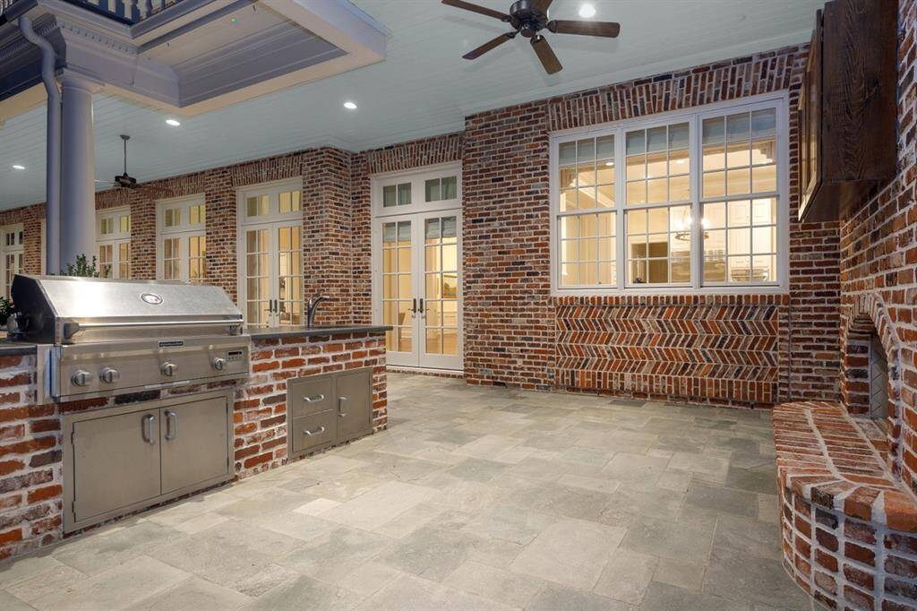 Evening photo of the Summer kitchen complete with Isokern gas fireplace, gas grill, and sink with pull-out faucet, textured Granite countertop, and plenty of storage. Outdoor sound system. Herringbone patterned brick under the windows of the kitchen.