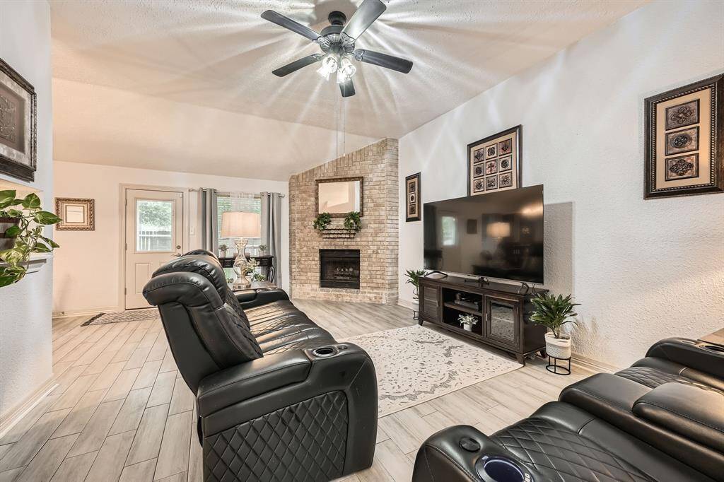 3106 Village Spring Ct. This inviting living room features a cozy brick fireplace, a modern ceiling fan, and sleek wood-look flooring with and abundant natural light.