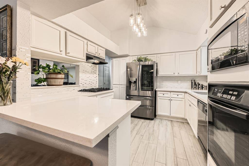3106 Village Springs Ct. This modern kitchen features sleek white cabinetry, stainless steel appliances, and a spacious layout. The room is brightened by elegant pendant lighting and offers ample counter space with a breakfast bar. The light wood flooring and open design create a welcoming atmosphere.