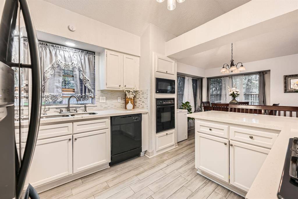 3106 Village Springs Ct. This kitchen features bright, white cabinetry with modern hardware and a sleek countertop. It includes built-in appliances, a double sink, and a cozy breakfast nook with large windows offering natural light. The tile flooring complements the overall clean and inviting look.