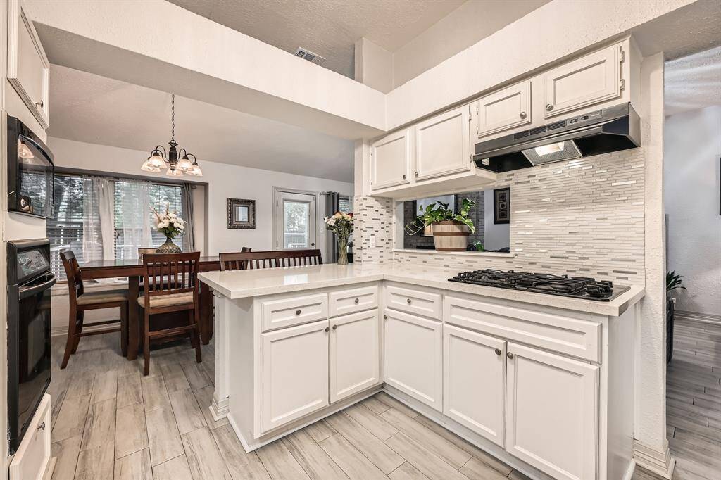 3106 Village Springs Ct. This inviting kitchen features white cabinetry, a sleek tile backsplash, and a modern cooktop. It opens to a cozy dining area with natural light and elegant wood flooring, creating a warm and functional space for family gatherings.