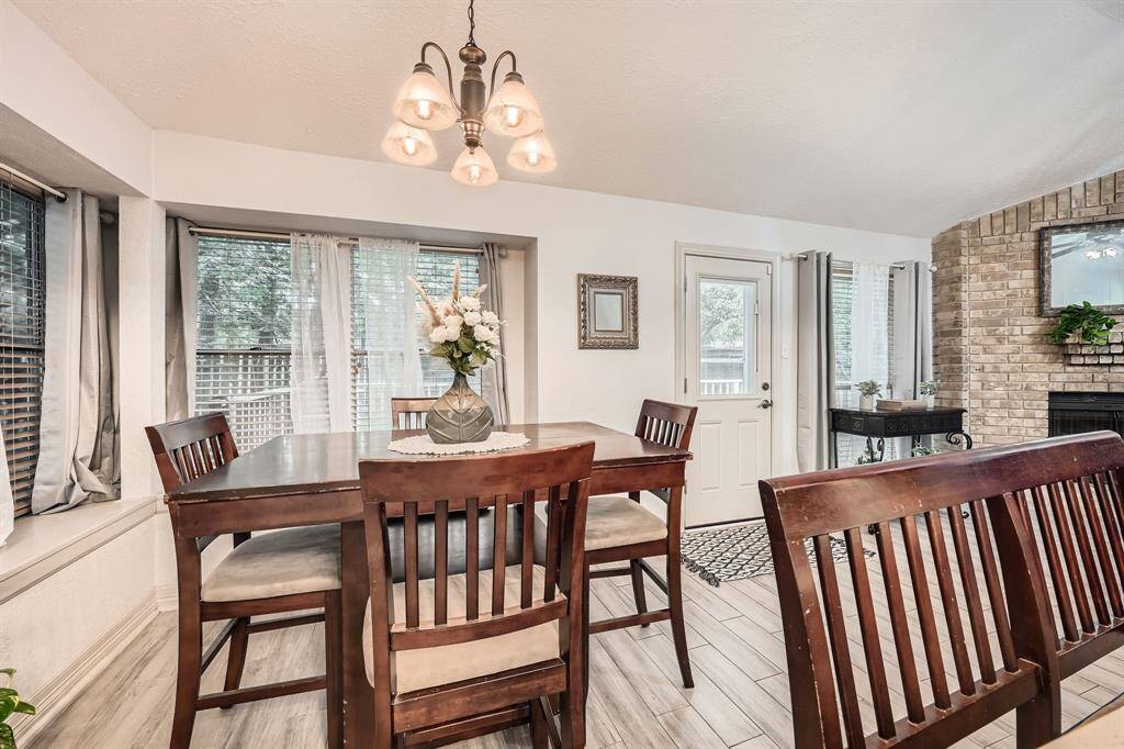 3106 Village Springs Ct. Bright dining area with large windows, wood-style flooring, and a cozy brick fireplace. And a stylish light fixture, creating a welcoming atmosphere.