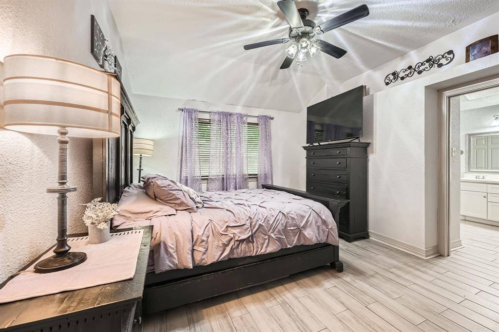 3106 Village Springs CT. This cozy primary bedroom features a vaulted ceiling with a ceiling fan, a large window, and opens to an en-suite bathroom, offering both comfort and convenience.