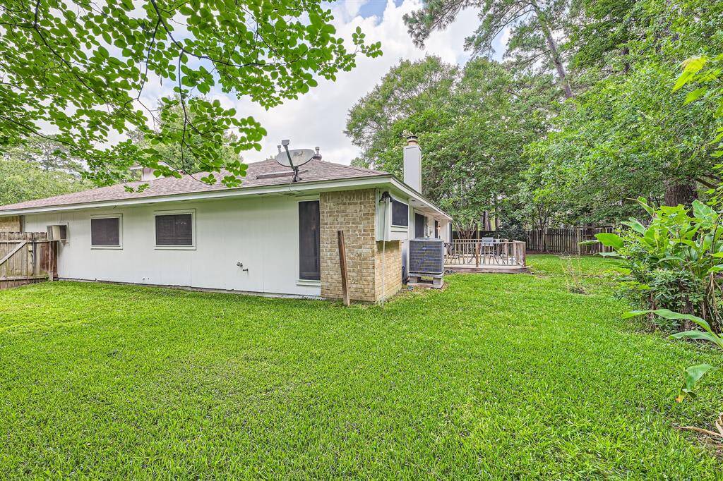 3106 Village Springs Ct  shows a cozy backyard featuring a well-maintained lawn, a small deck with seating, and plenty of surrounding greenery for privacy. The house has a brick and siding exterior with a fenced perimeter, providing a serene outdoor space.