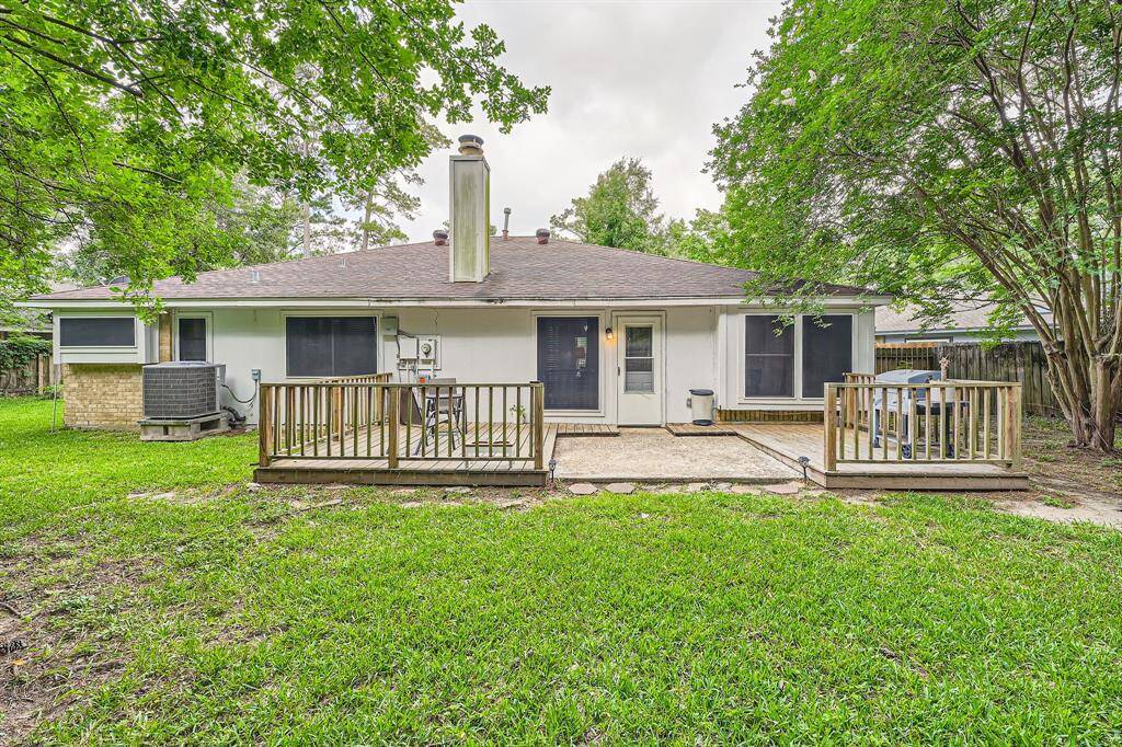 3106 Village Springs Ct. shows a cozy single-story home with a spacious backyard. It features a wooden deck perfect for outdoor gatherings, surrounded by lush green grass and mature trees, providing a serene and private setting.