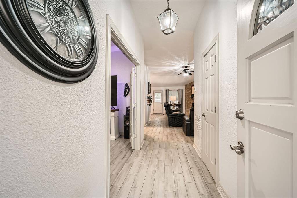 3106 Village Springs CT showcases a welcoming entry hallway with light wood flooring and modern lighting. It leads to a cozy living area with visible seating and a ceiling fan, offering a glimpse into a well-lit, comfortable space.
