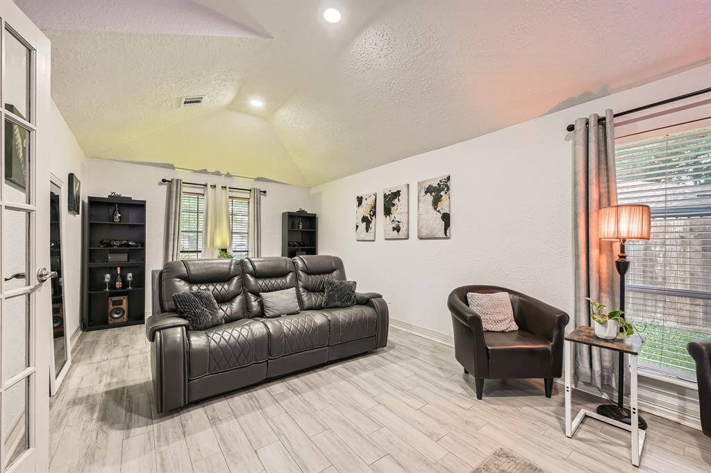 3106 Village Springs CT is inviting living room features a vaulted ceiling, modern tile flooring, and ample natural light from large windows. making it a cozy space for relaxation.