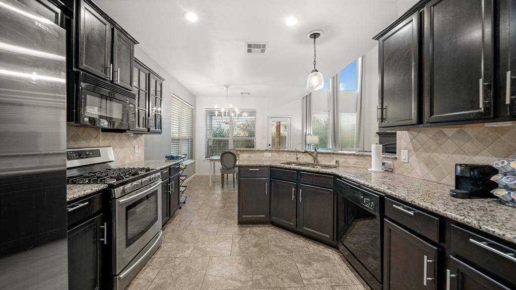 Features include granite countertops paired with a coordinating stone backsplash, stainless steel appliances, rich cabinets with updated hardware, under cabinet lighting, recessed lighting, and breakfast bar seating.