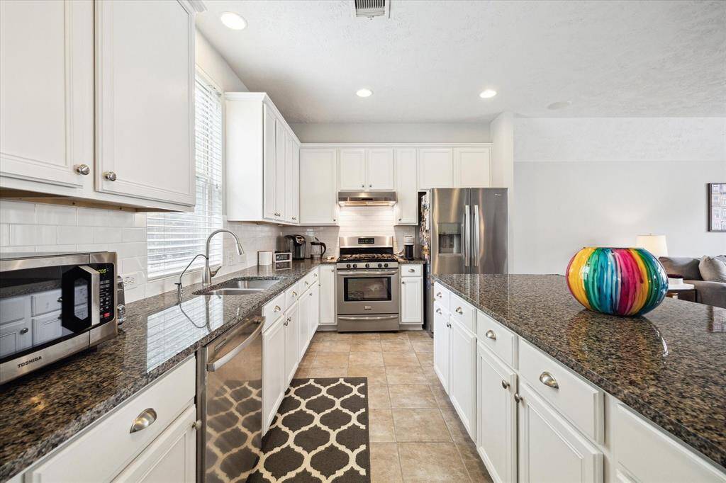The kitchen is a chef's delight, equipped with a complete package of stainless steel appliances, a sleek white subway tile backsplash, granite countertops, and a spacious island that seamlessly connects to the large living area. This setup is perfect for hosting gatherings and enjoying everyday meals.