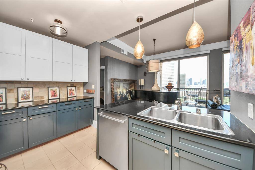 This modern kitchen features sleek two-tone cabinetry, a double sink, and stylish pendant lighting. It opens to a bright living area with large windows offering city views, creating an inviting and functional space.