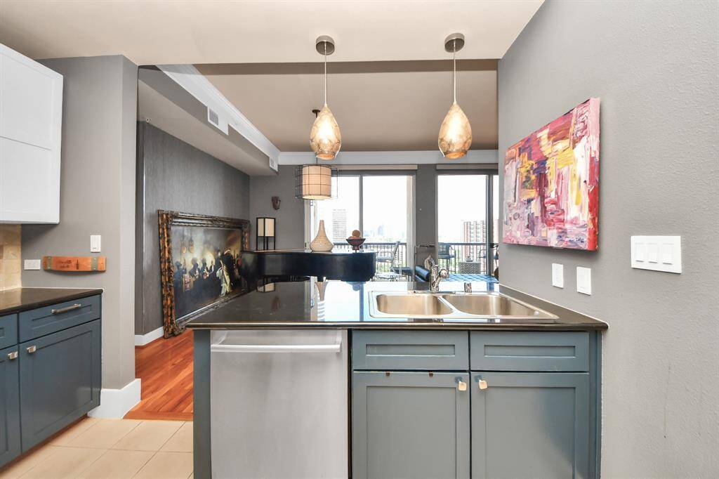 This modern kitchen features sleek cabinetry, a double sink, and pendant lighting. The open layout connects to a bright living area with large windows and a balcony view, offering a stylish and functional space.
