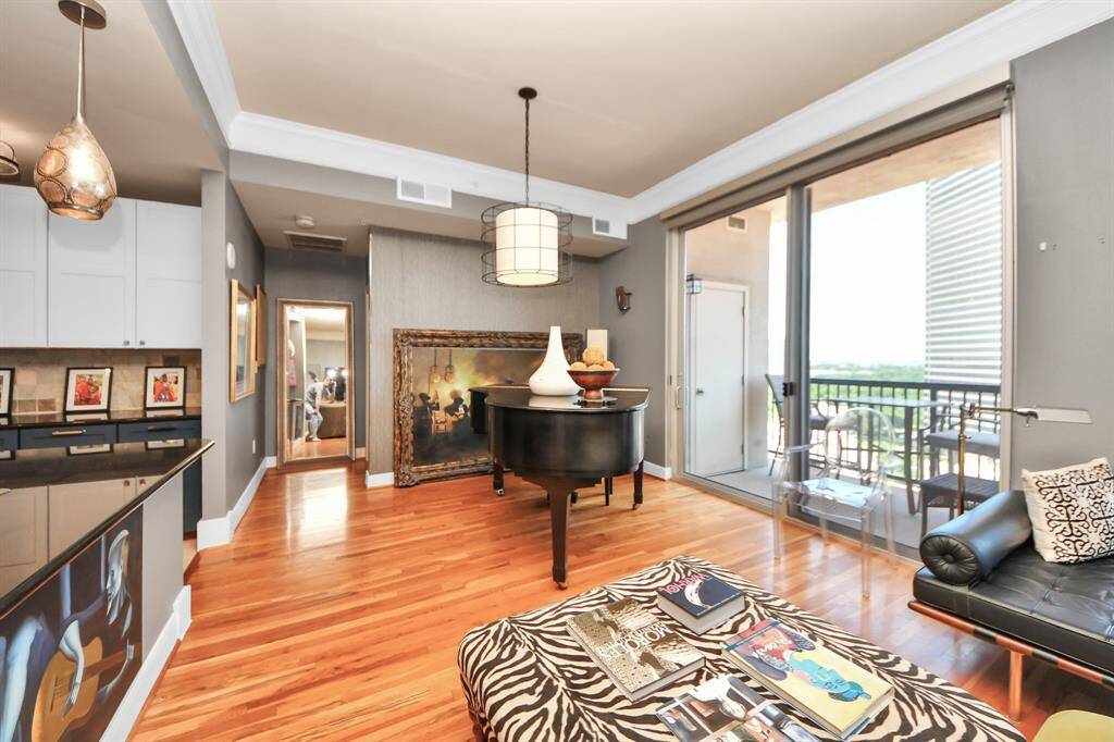 This modern living space features hardwood floors, ample natural light from large windows, and a cozy seating area. The open layout seamlessly connects to a stylish kitchen, and there's access to a balcony with outdoor seating.