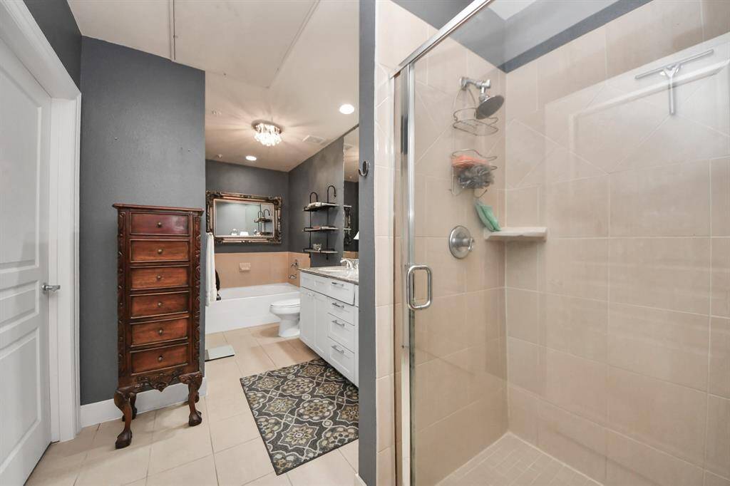 This is a stylish bathroom featuring a glass-enclosed shower, elegant dark walls, and a dual-sink vanity. A vintage-style chest and a decorative mirror add character, while a patterned rug enhances the space's warmth and charm.