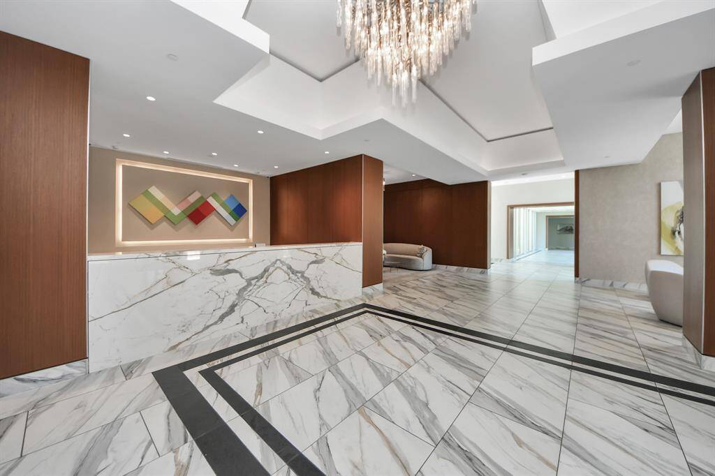 This photo showcases a modern, elegant lobby with marble flooring and walls, featuring a striking chandelier and contemporary artwork. The space is well-lit and inviting, blending luxury and style seamlessly.
