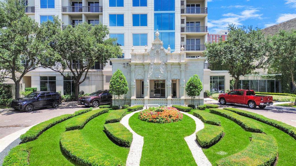 This photo showcases a luxurious residential building with elegant architecture and well-maintained landscaping. The entrance features a grand facade and a circular driveway lined with lush greenery and colorful flower beds.