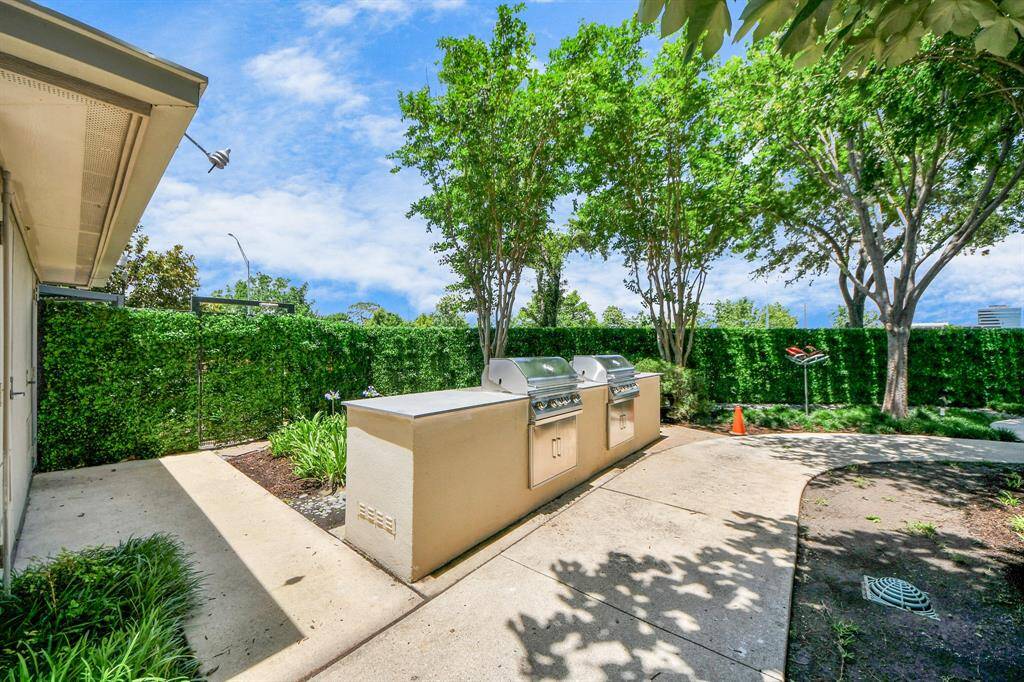 This photo showcases a spacious outdoor area featuring a built-in grill station, surrounded by lush greenery and mature trees, providing a perfect setting for outdoor cooking and entertaining.