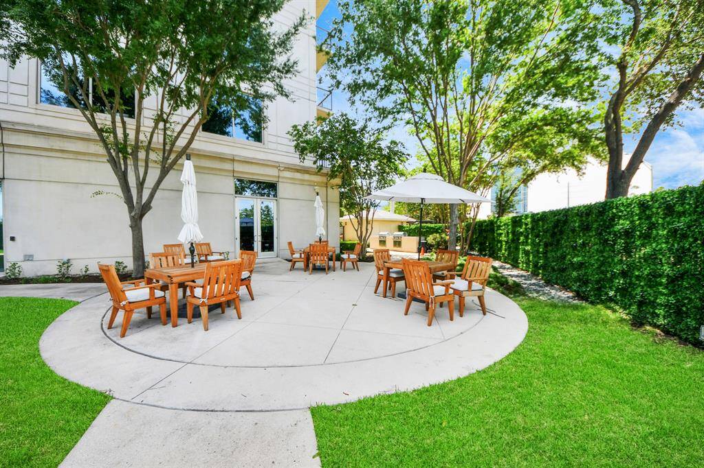 This photo showcases a spacious outdoor patio area with wooden seating and tables, surrounded by lush greenery and mature trees, ideal for relaxation and social gatherings.