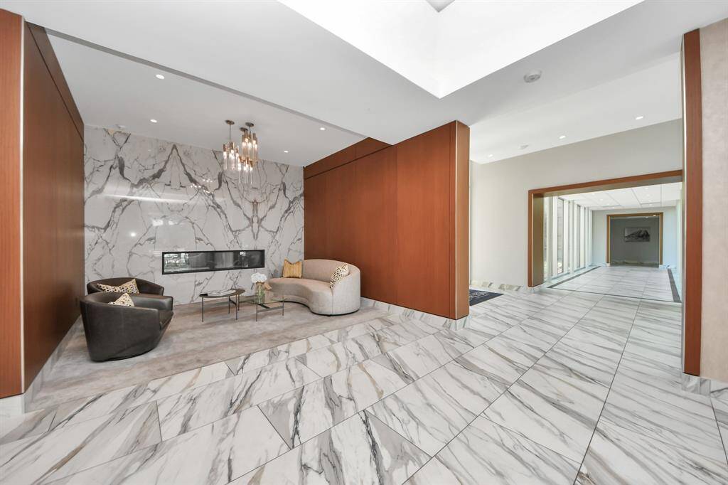 This photo showcases a modern, elegant living space with a marble accent wall, sleek fireplace, and stylish sitting area. The room features large floor tiles and warm wood paneling, creating a sophisticated and inviting atmosphere.