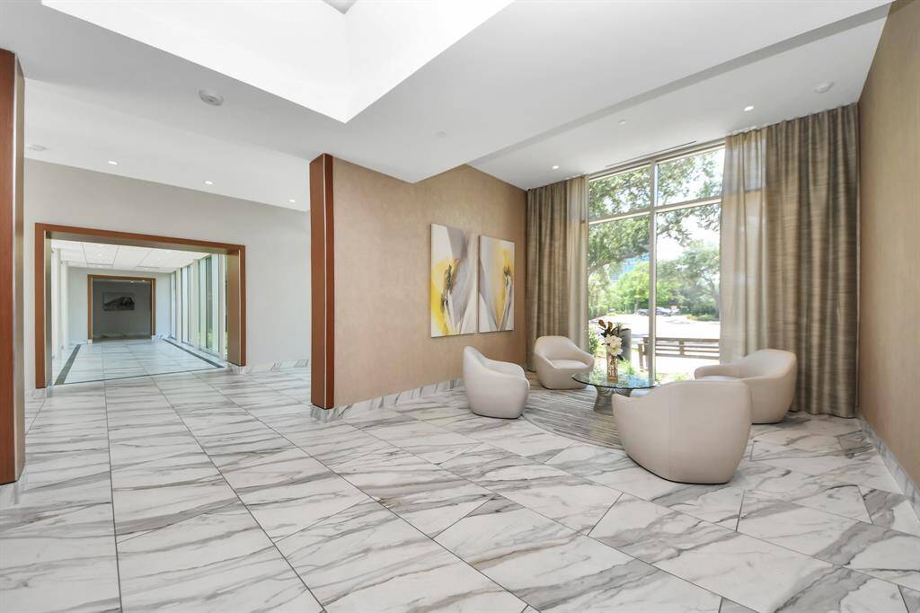 This photo shows a modern, elegant lobby with large windows offering plenty of natural light. It features marble flooring, contemporary seating, and tasteful artwork, creating a welcoming and upscale environment.