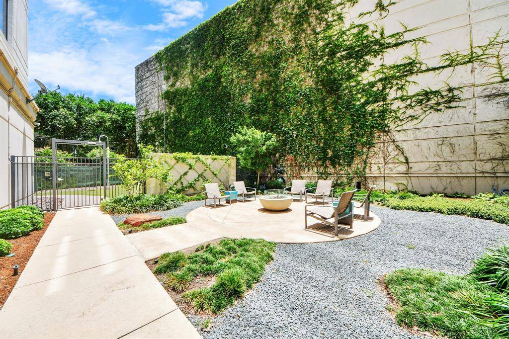 This photo showcases a serene outdoor patio area featuring a circular seating arrangement around a fire pit. It's surrounded by lush greenery and ivy-covered walls, offering a private and inviting space for relaxation or entertaining.