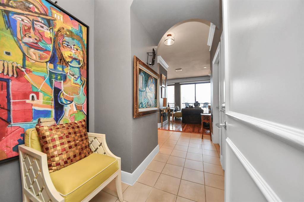 This welcoming entryway features modern tile flooring and vibrant artwork. It leads into a bright, open living space with hardwood floors and ample natural light from a large window.
