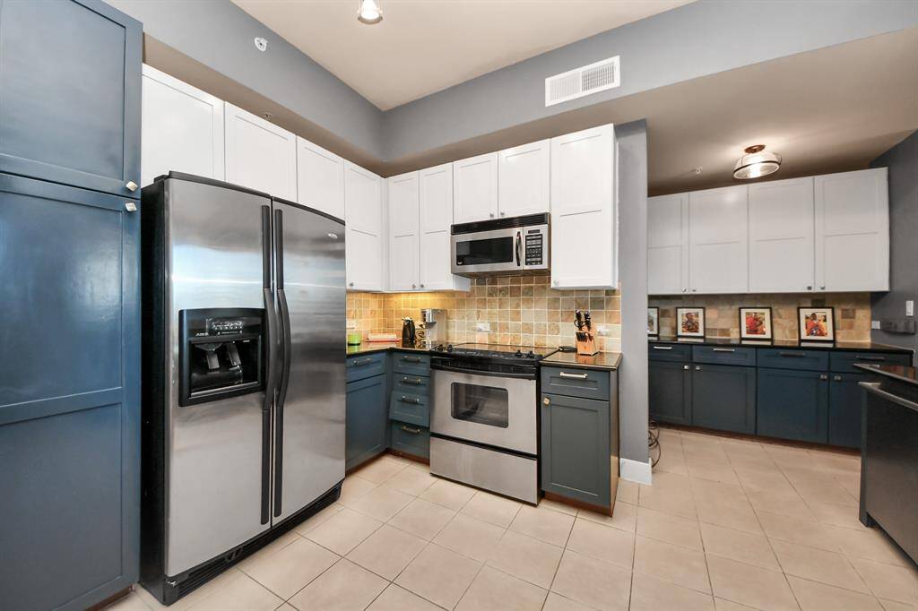This kitchen features modern stainless steel appliances, a mix of white and dark blue cabinetry, and a tiled backsplash. The space is open with ample counter space, providing a functional and stylish cooking area.