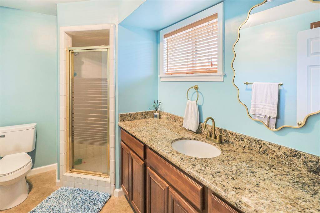 The primary full bathroom ensuite features a corner standing shower, granite countertops and a continued coastal charm aesthetic.