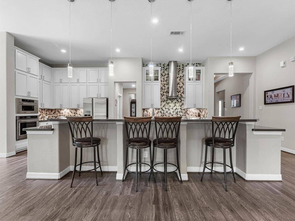 This light and bright kitchen features a large quartz island, white cabinets, a large sink overlooking your family room, recessed lighting, additional pendant lighting, and beautiful backsplash.
