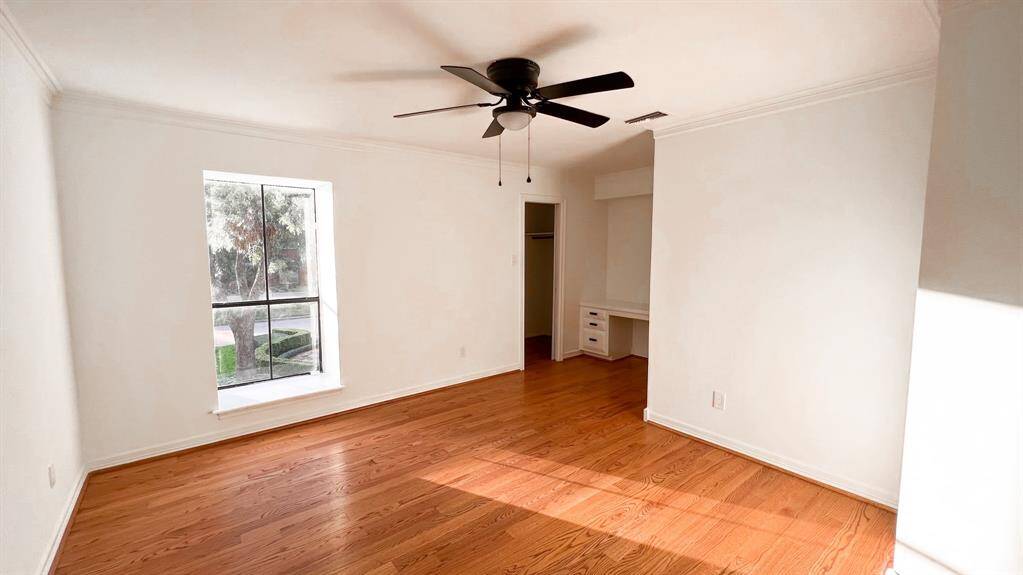 This secondary bedroom sits on the second floor and features elegant wood flooring, a thoughtfully placed window to allow natural light while preserving privacy, abundant closet space, and a built-in desk.