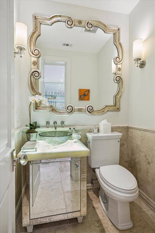 Just off the Front Entry is the formal POWDER ROOM with its travertine tile flooring, furniture style cabinet with raised glass bowl/under lit onyx counter/wall mounted fixtures, framed mirror, recessed lighting, 2 wall-mounted decorative light sconces, painted walls with stone tile wainscotting.